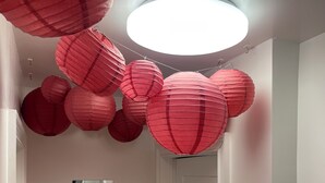 A hallway with a white door, red paper lanterns hanging from the ceiling, and a ceiling light.