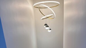 A modern staircase with wooden steps and a glass railing, leading to a landing with a unique circular light fixture. - Family Vacation Modern Norwood  (Norwood)