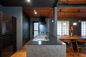 Una cucina moderna con isola centrale, soffitto in legno e zona pranzo con tavolo e sedie in legno.