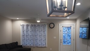 Ein Wohnzimmer mit einem dunkelgrauen Sofa, einem Holztisch, einer Arbeitsplatte aus Granit, einer Wanduhr und einer Tür mit Milchglasfenstern.
