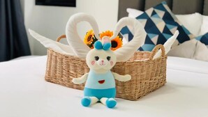 A plush toy rabbit in a wicker basket on a bed with a geometric pillow and a plain wall in the background. - Cher Cher Pool villa (Ban Chang)