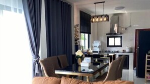 A modern living room with a brown sofa, a dining table with chairs, and a kitchen in the background. - Cher Cher Pool villa (Ban Chang)