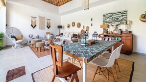 A spacious living area with a high ceiling, a dining table with chairs, a sofa, and a fan.