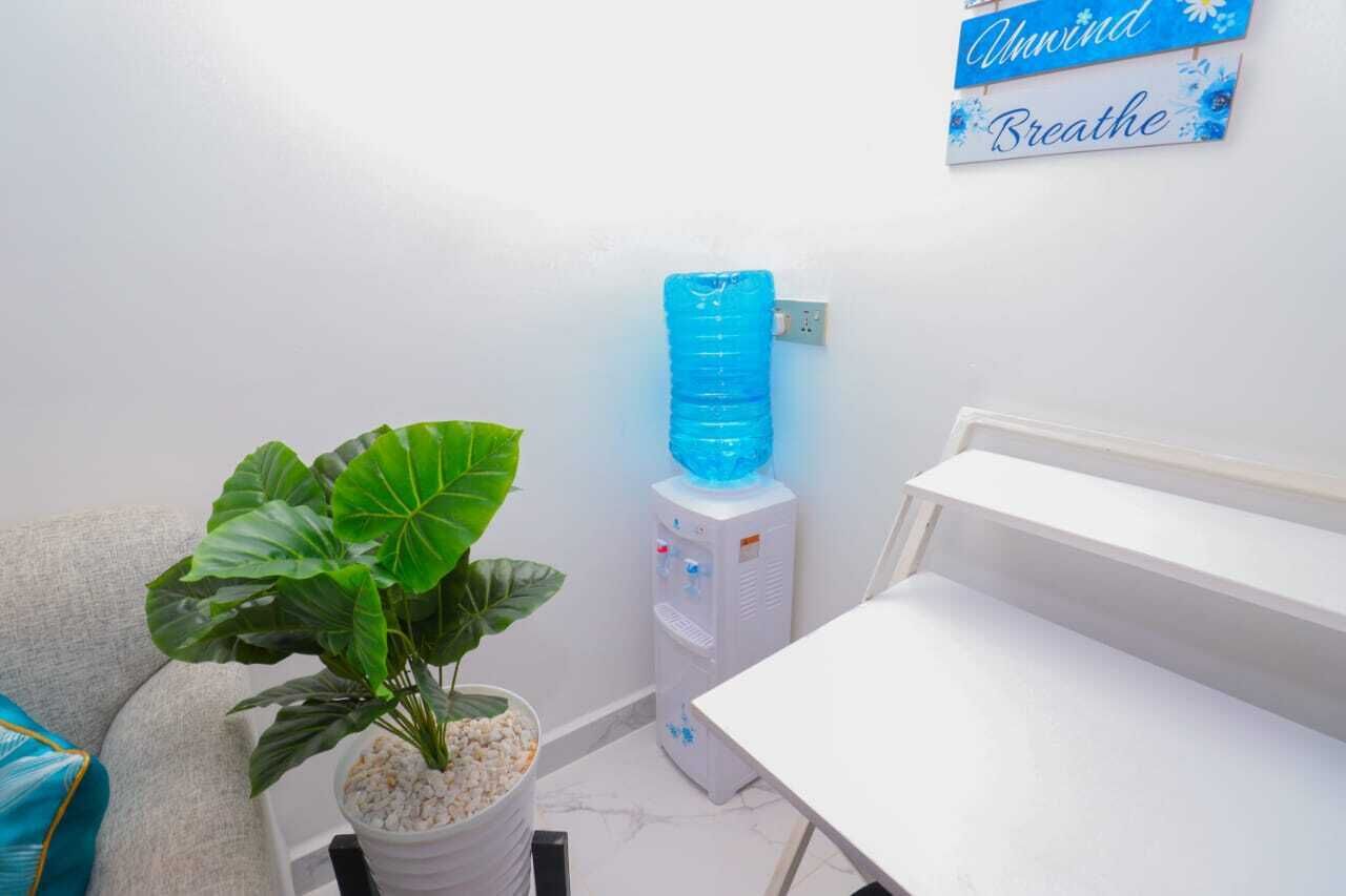 A small room with a white table, a water dispenser, a potted plant, and a sign on the wall.