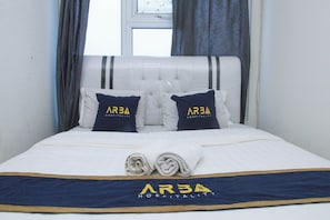 A neatly made bed with two pillows, a folded towel, and a bedspread with the logo "AR3A Hospitality". - ARBA Sentra Timur Tower Sapphire (Jakarta)