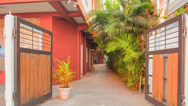A narrow alleyway with a red building, wooden gates, and potted plants. - Naksha Tree Hotels Honey Crest (Chennai)