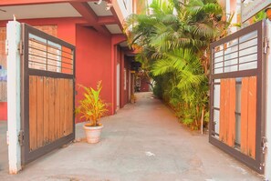 A narrow alleyway with a red building, wooden gates, and potted plants. - Naksha Tree Hotels Honey Crest (Chennai)