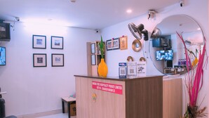 A reception desk with framed pictures on the wall, a mirror, and a sign indicating the hotel's name and GST rate. - Naksha Tree Hotels Honey Crest (Chennai)