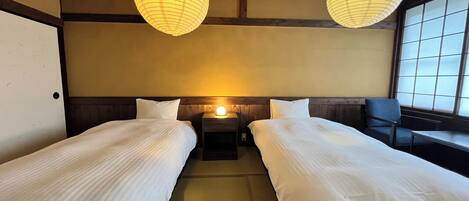 A hotel room with two single beds, a nightstand with a lamp, a chair, and a large window.