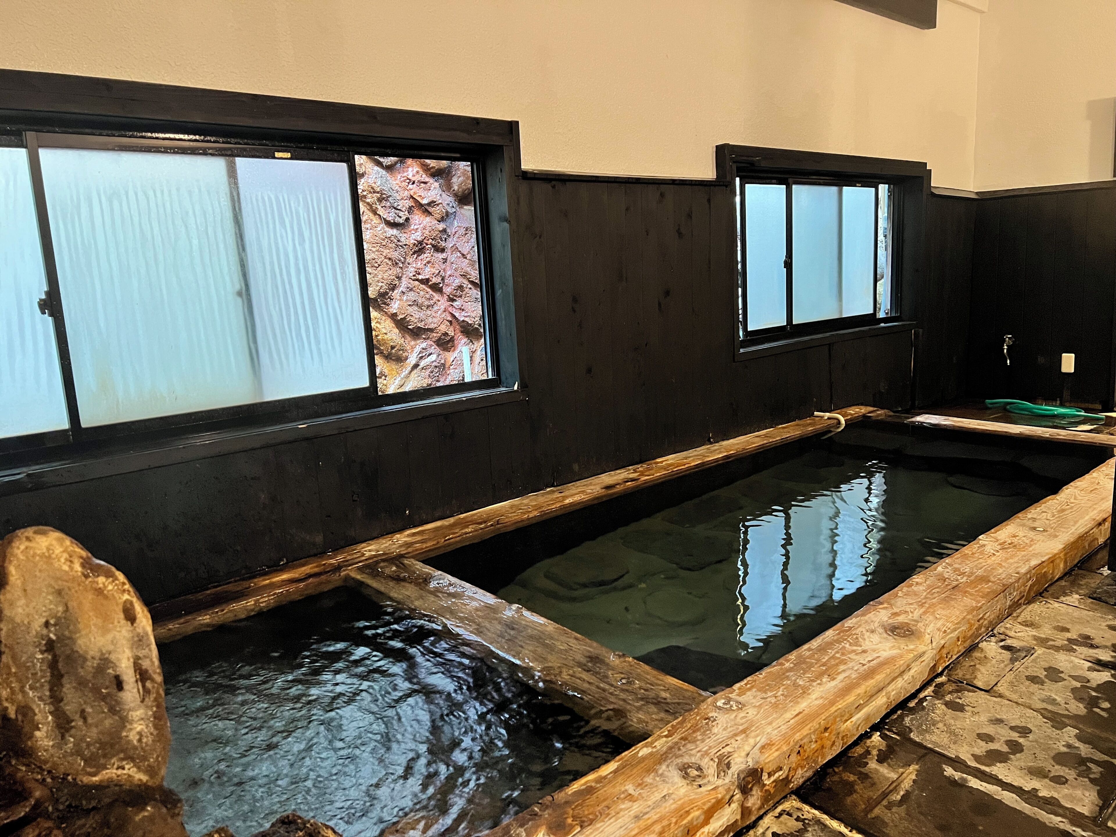 Un onsen japonés tradicional con tinas de madera y paredes de piedra.