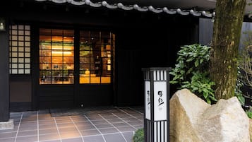 Entrada de un edificio japonés tradicional con suelo de baldosas, una puerta negra con paneles de vidrio y un farol de piedra.