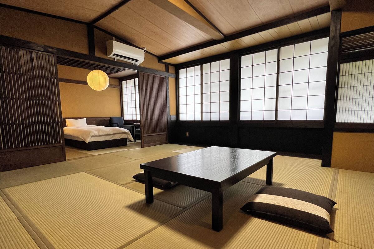 Una stanza tradizionale giapponese con pavimento in tatami, un tavolino, un letto e porte scorrevoli.