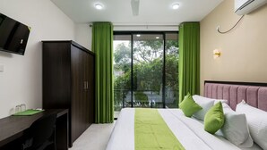 Quarto de hotel com cama, escrivaninha, guarda-roupa e televisão.