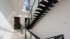 Um interior moderno com escada de vidro, paredes brancas e porta que dá acesso a outro cômodo.