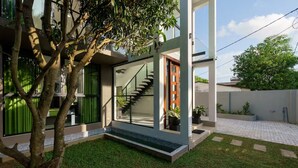A modern house with a glass staircase, a green lawn, and a tree in the foreground. - Green Vibe -Two Bedroom Pool View Apartment in Colombo (Nugegoda)