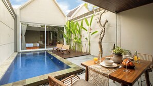 A modern outdoor pool area with a dining table set for two, surrounded by comfortable seating and lush greenery. - Damarya Villa Canggu (Canggu)