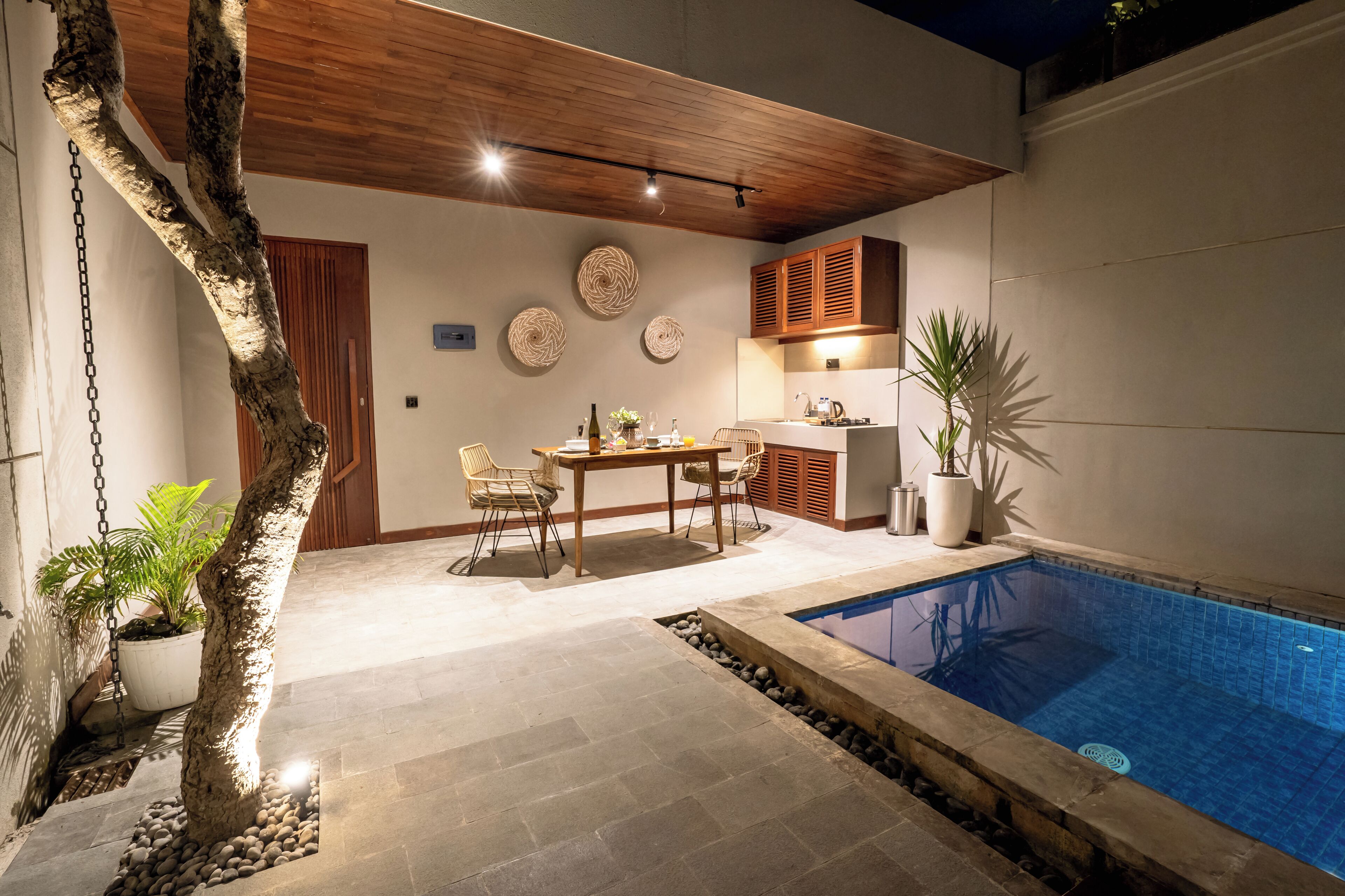 Un espace aménagé au bord de la piscine, comprenant une table et des chaises, un plafond en bois et un petit coin cuisine avec des placards.
