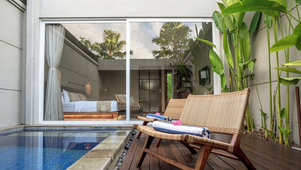 A poolside area with wicker lounge chairs, a glass-enclosed bedroom with a bed, and tropical plants. - Damarya Villa Canggu (Canggu)