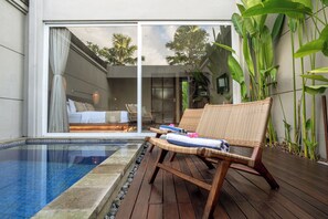A poolside area with wicker lounge chairs, a glass-enclosed bedroom with a bed, and tropical plants. - Damarya Villa Canggu (Canggu)