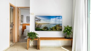 Una habitación moderna con un ventanal grande, un banco de madera, una planta en maceta y un cuadro de un paisaje costero.