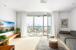 A modern living room with a balcony, a grey sofa, a wooden bench, and a large painting. - Stylish Apt Balcony View by Sea N' Rent (Tel Aviv)