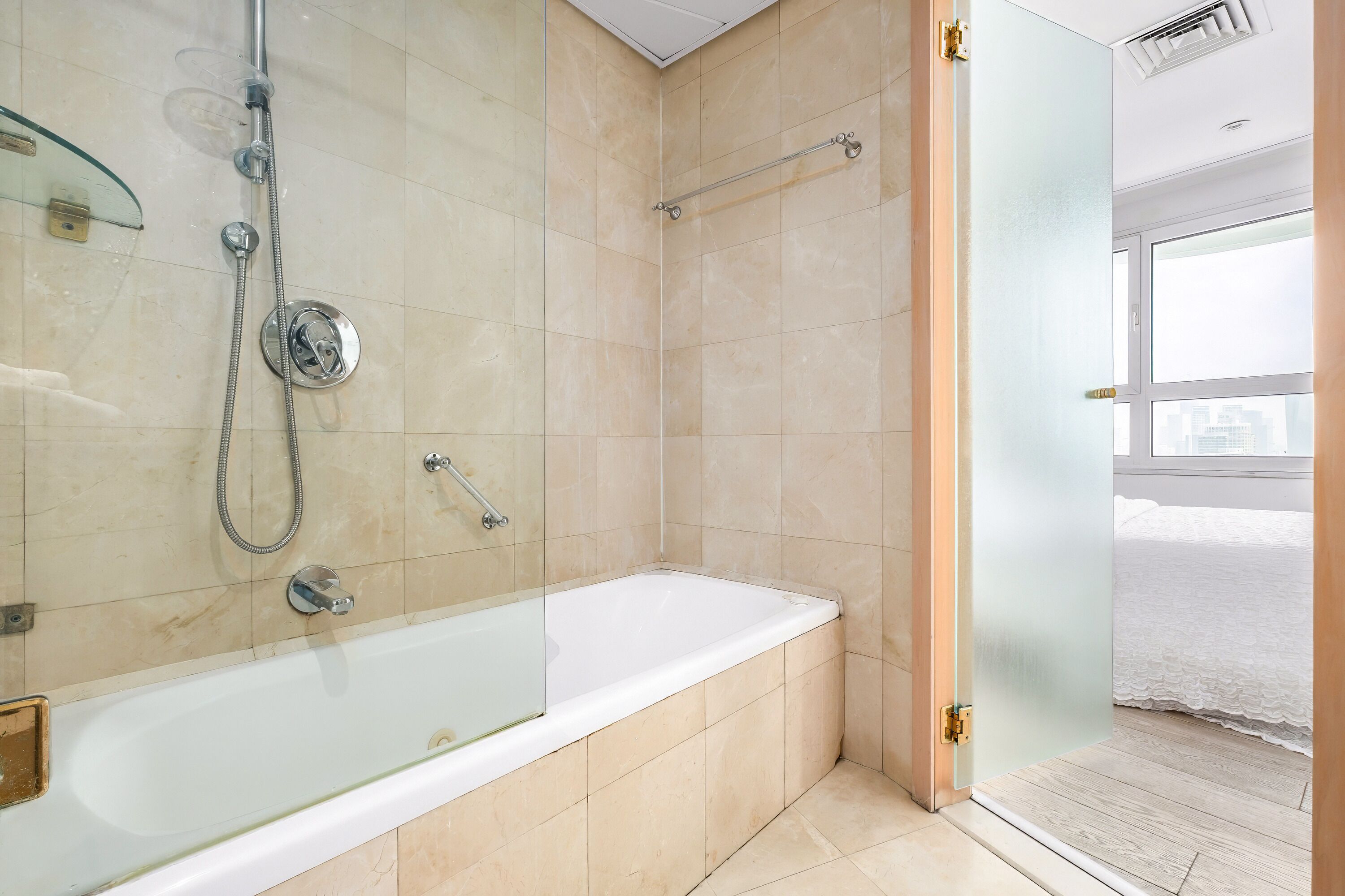 A modern bathroom with a glass-enclosed shower, a standalone bathtub, and a glass door leading to a bedroom.