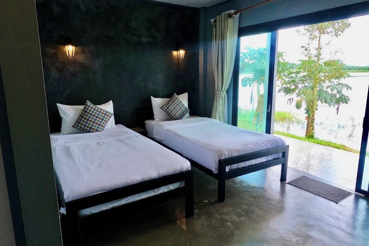 A room with two beds, dark walls, and a view of greenery outside.