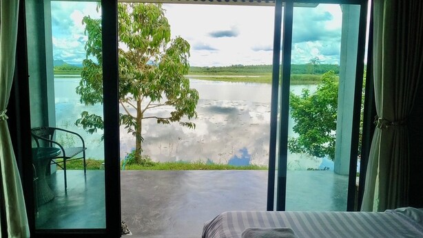 A room with a bed, a chair, and a view of a lake with trees. - OYO 75530 By the dam cafe and farmstay (Plai Phraya)