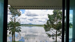 A view from a covered area overlooking a calm lake with trees and distant mountains. - OYO 75530 By the dam cafe and farmstay (Plai Phraya)