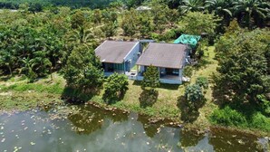 A two-story building with a flat roof, surrounded by lush greenery and a body of water. - OYO 75530 By the dam cafe and farmstay (Plai Phraya)
