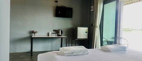 Habitación de hotel con cama, una mesita con tetera, televisión y refrigerador.