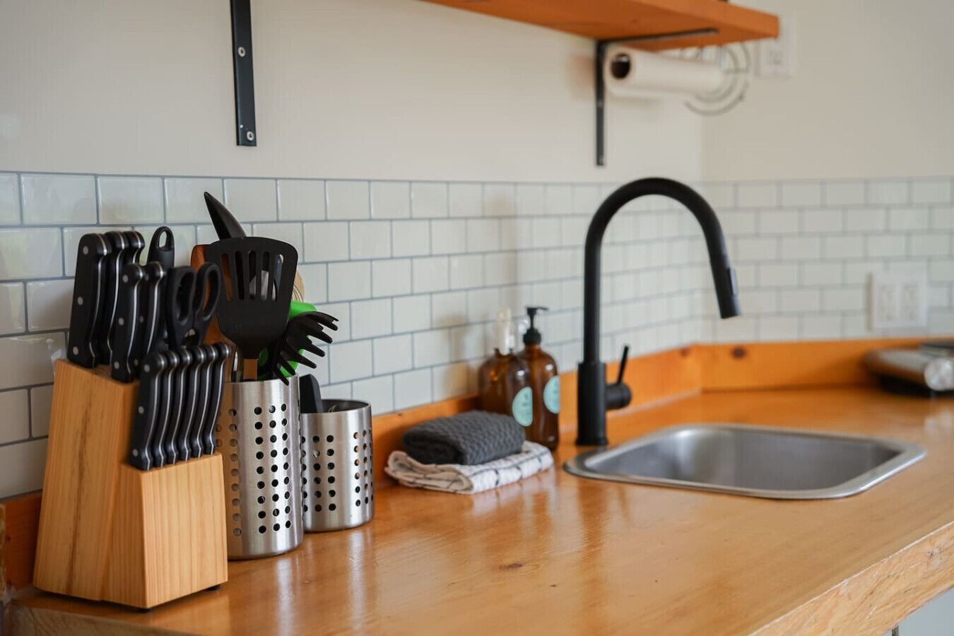 Una cocina con encimera de madera, pileta de acero inoxidable y distintos utensilios en organizadores.