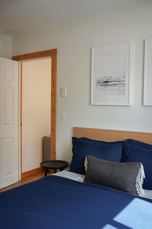 Een slaapkamer met een bed, een klein rond tafeltje en een deur naar een andere kamer.