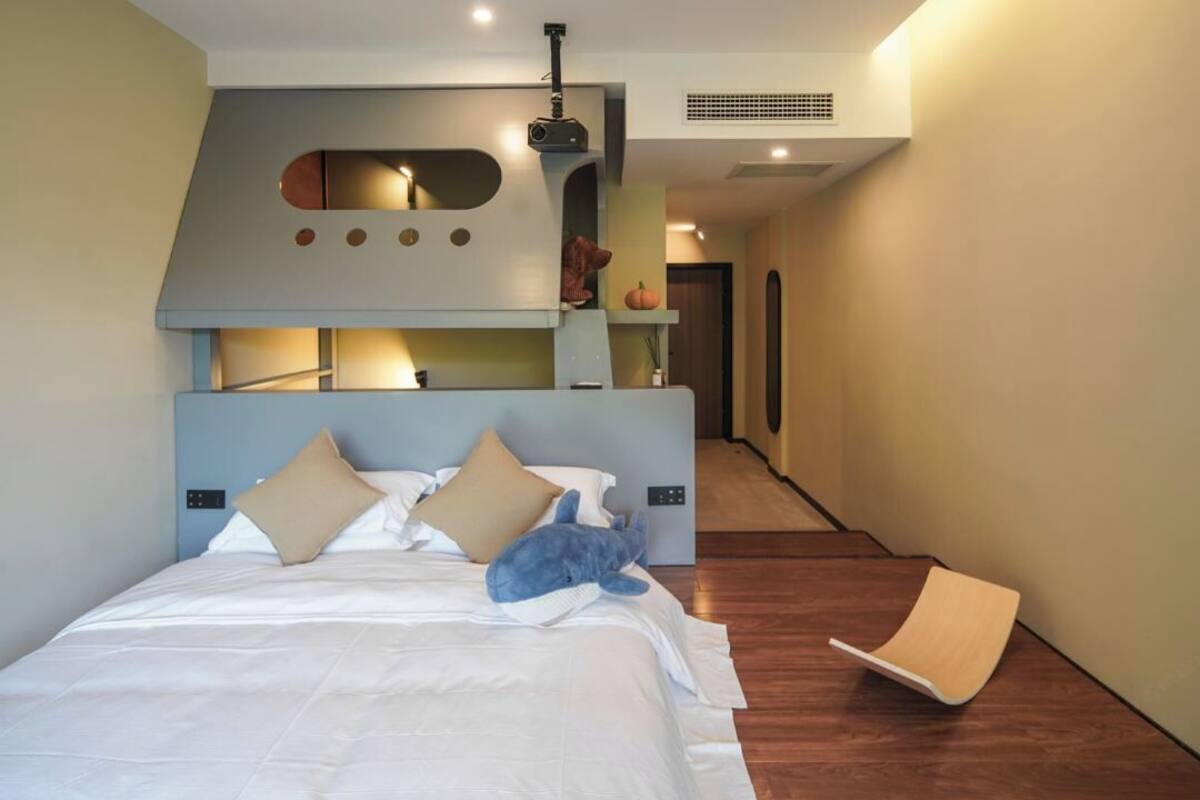 A modern hotel room with a large bed, a built-in TV, and a unique ceiling design.