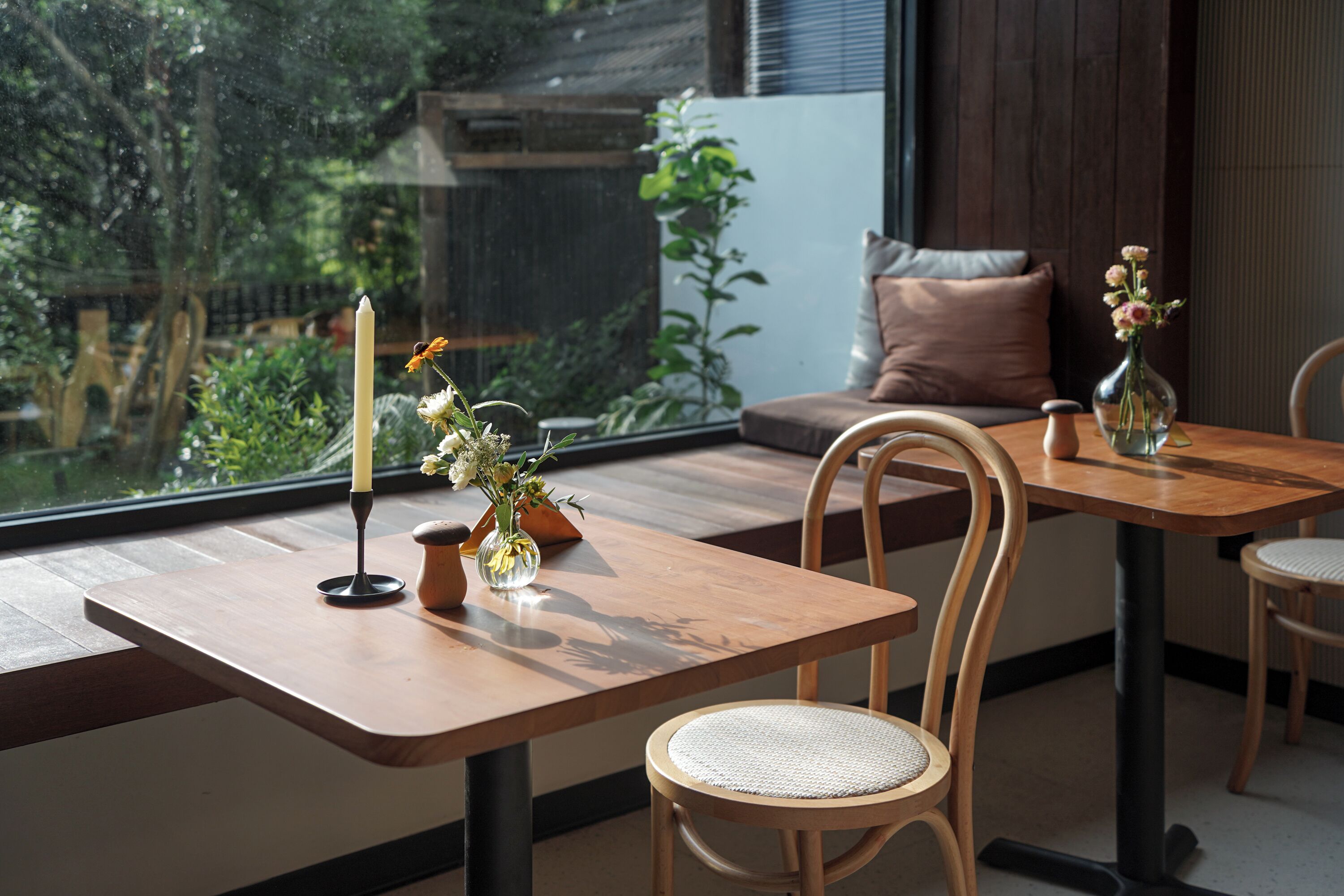 Un espace repas avec des tables et des chaises en bois, une bougie et un vase rempli de fleurs.