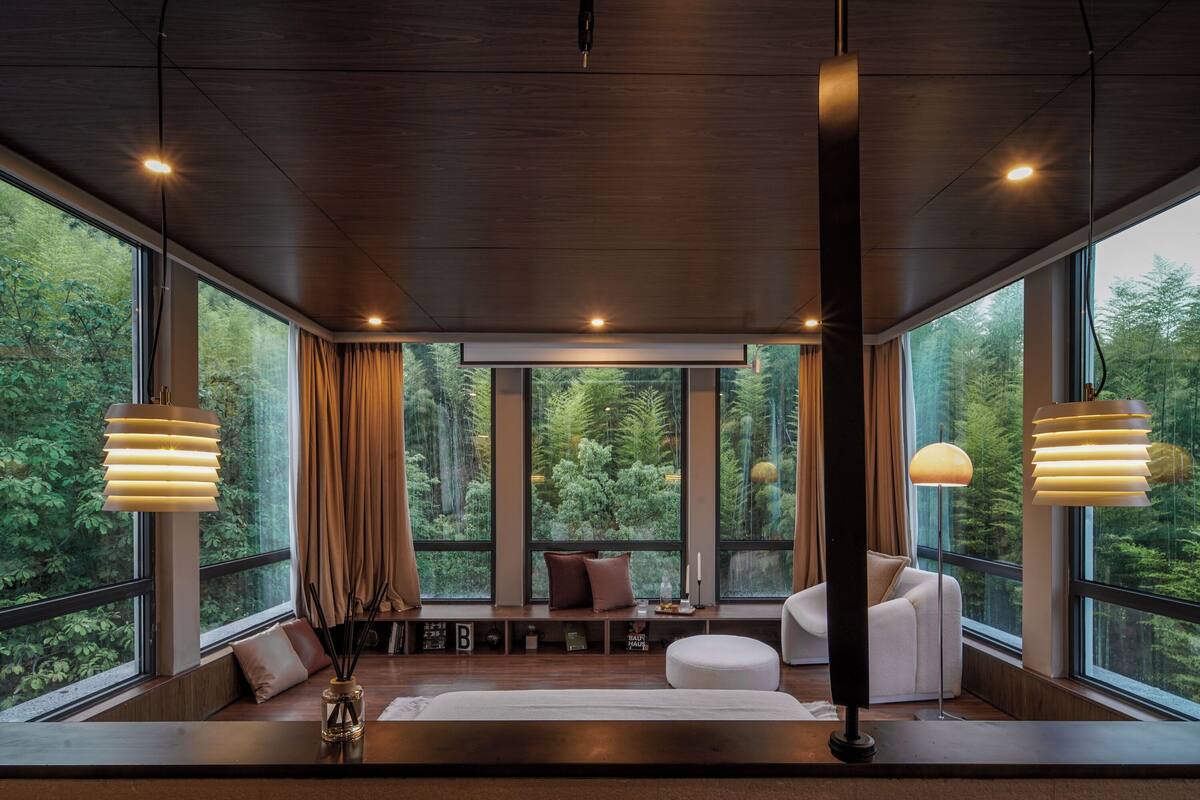 A modern room with large windows, a sofa, a bench, and a lamp.