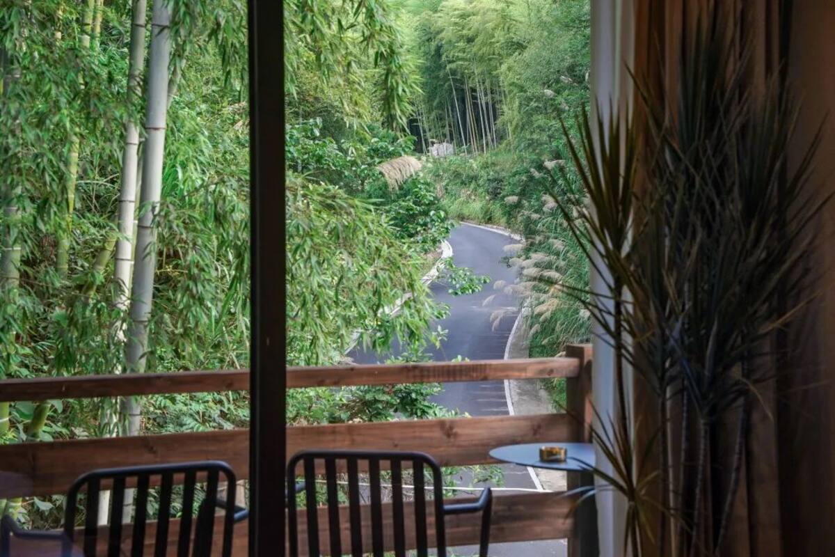 A balcony with a view of a winding road through a lush green landscape, featuring bamboo and other vegetation.