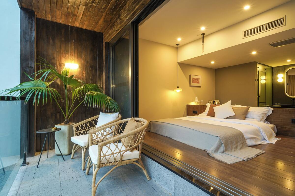 A modern bedroom with a large bed, a sitting area with a chair, and a potted plant.