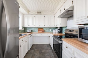 A kitchen with white cabinets, a green backsplash, a wooden countertop, a stainless steel refrigerator, a black oven, and a microwave.