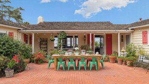 A covered patio with a brick floor, a wooden table with chairs, and potted plants.