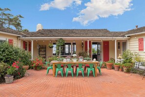 Un patio cubierto con suelo de ladrillo, una mesa de madera con sillas y plantas en macetas.