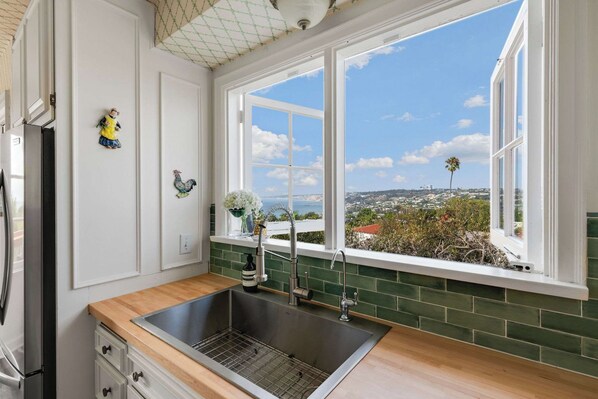 Una cocina con un ventanal amplio, un lavamanos de acero inoxidable y vistas a un paisaje urbano.