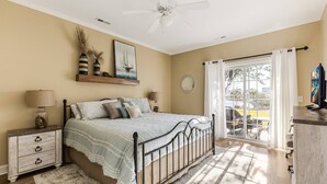 A bedroom with a bed, nightstand, dresser, and a view of the outdoors through a sliding glass door.