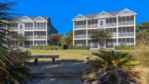 A beachfront property with a wooden deck, two-story buildings, and a clear blue sky.