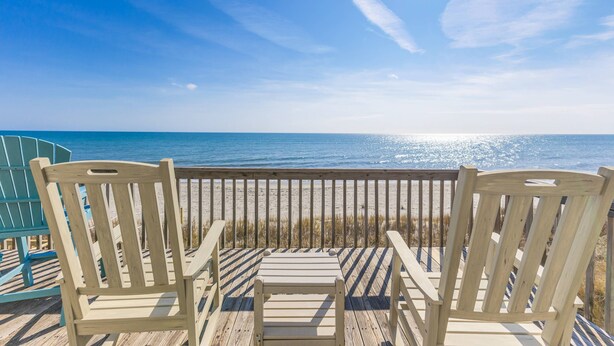 Een houten terras met twee stoelen gericht op het strand.
