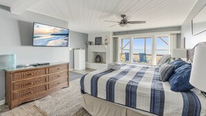 Een slaapkamer met een groot bed, een plafondventilator, een televisie en uitzicht op de oceaan.