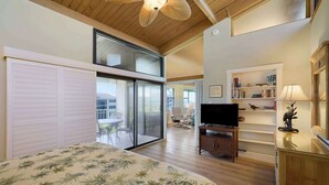 A bedroom with a bed, a TV, a bookshelf, and a sliding glass door leading to a balcony. - Loggerhead 523 | Beachfront Condo with Vaulted Ceilings | Steps to the Sand (Sanibel)