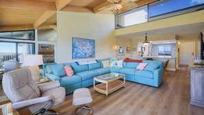 A spacious living area with a blue sofa, a chair, a coffee table, and a ceiling fan. - Loggerhead 523 | Beachfront Condo with Vaulted Ceilings | Steps to the Sand (Sanibel)