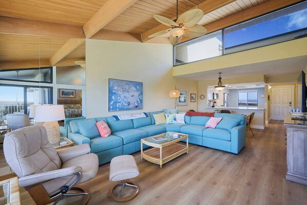 A spacious living area with a blue sofa, a chair, a coffee table, and a ceiling fan. - Beachfront Condo at Loggerhead Cay with Vaulted Ceilings (Sanibel)
