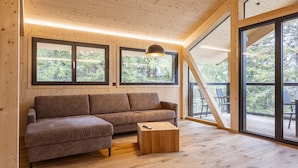 Un intérieur moderne avec un plancher en bois, un canapé marron, une table basse en bois et de grandes fenêtres donnant sur un paysage verdoyant.